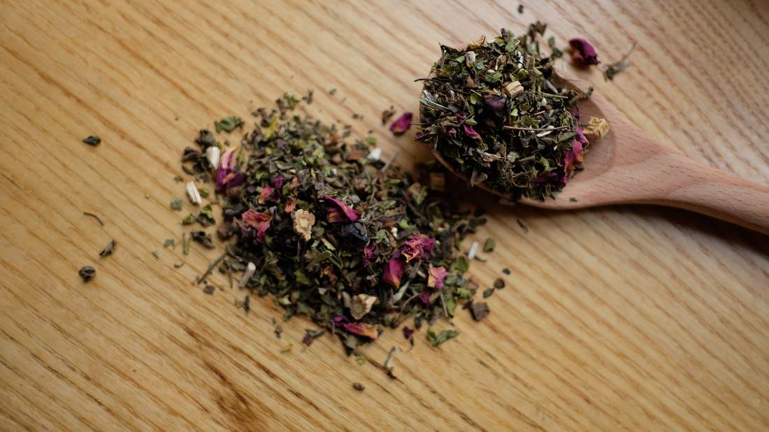 Loose herbal tea scattered with dried rose petals on a wooden spoon